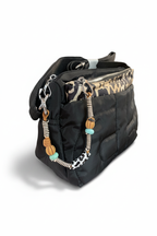 Bolso bandolera acolchado negro, vista lateral con colgantes de cuentas